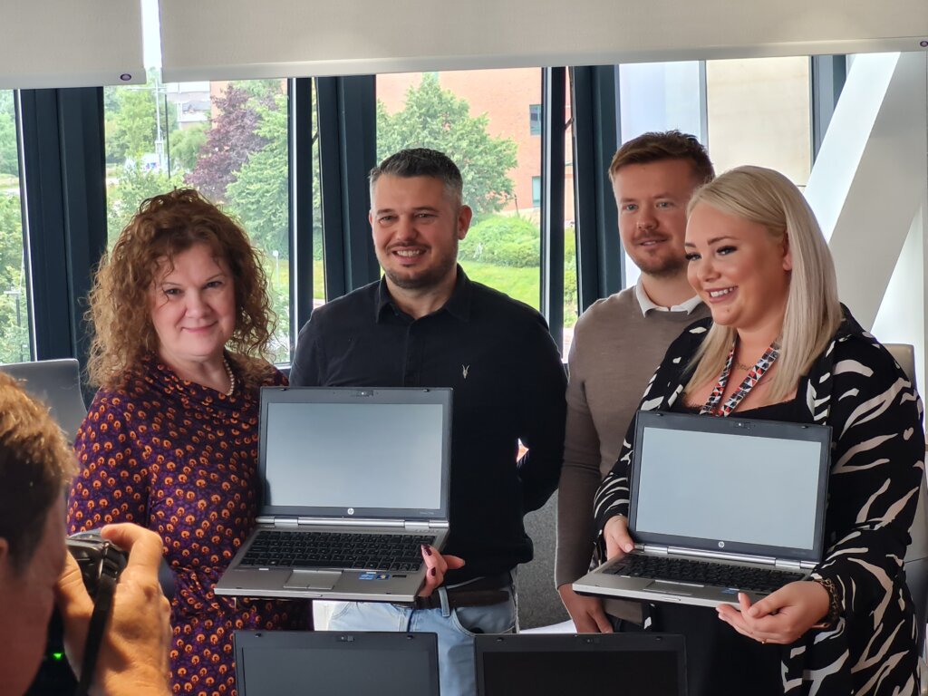 Four people (two men and women) are  holding laptops and smiling