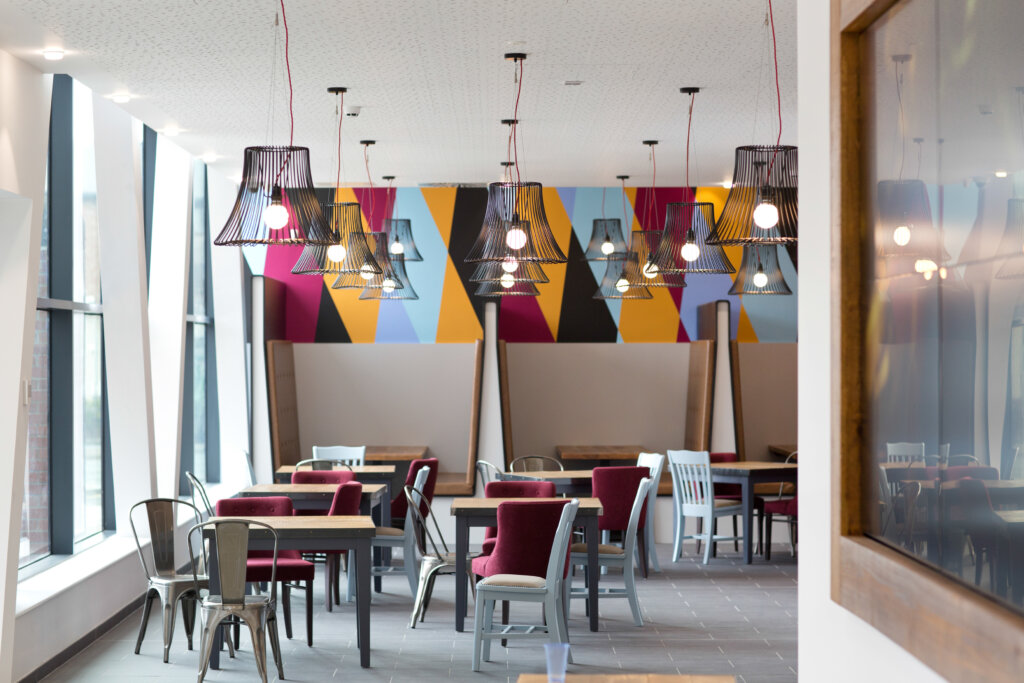 A cafe space with colourful painting wall, many tables and red chairs